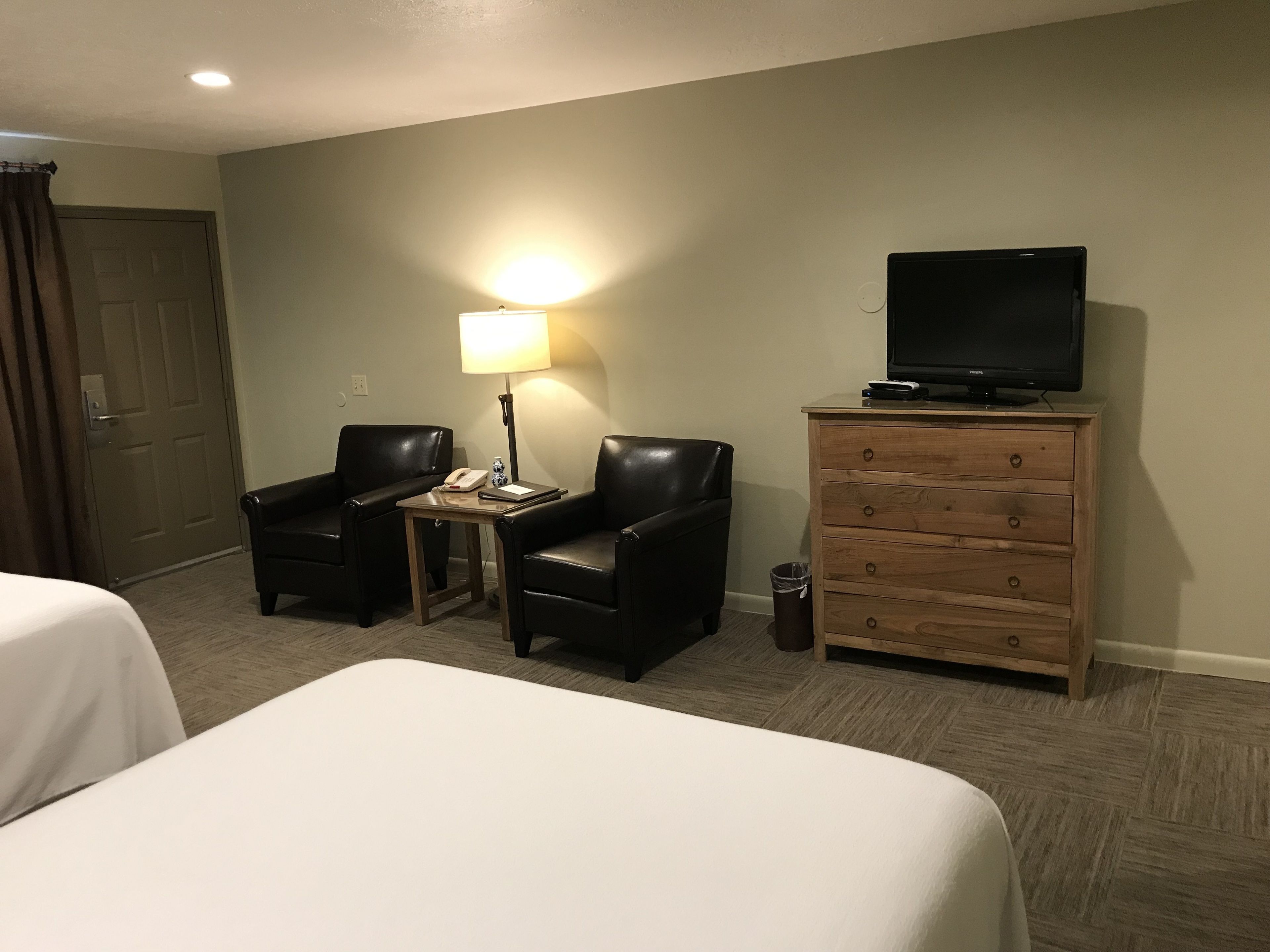 Een hotelkamer met twee bedden, een bureau met een lamp, een televisie op een dressoir en een deur.
