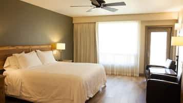 Une chambre d’hôtel avec un grand lit, un ventilateur de plafond, un bureau avec une chaise et une fenêtre avec des rideaux.