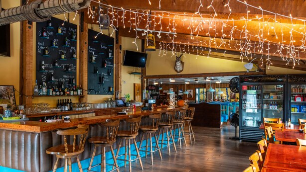 A bar area with wooden bar stools, a counter with bottles, and a television mounted on the wall. - Yosemite Westgate Lodge (Groveland)