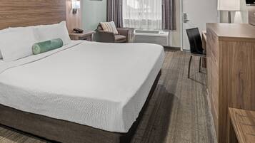A hotel room with a large bed, a desk, a chair, a lamp, and a TV.