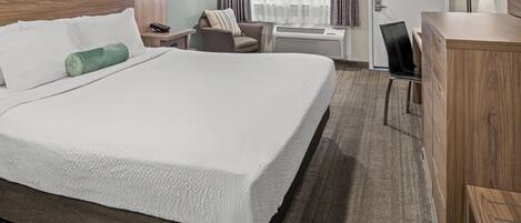 A hotel room with a large bed, a desk, a chair, a lamp, and a TV.