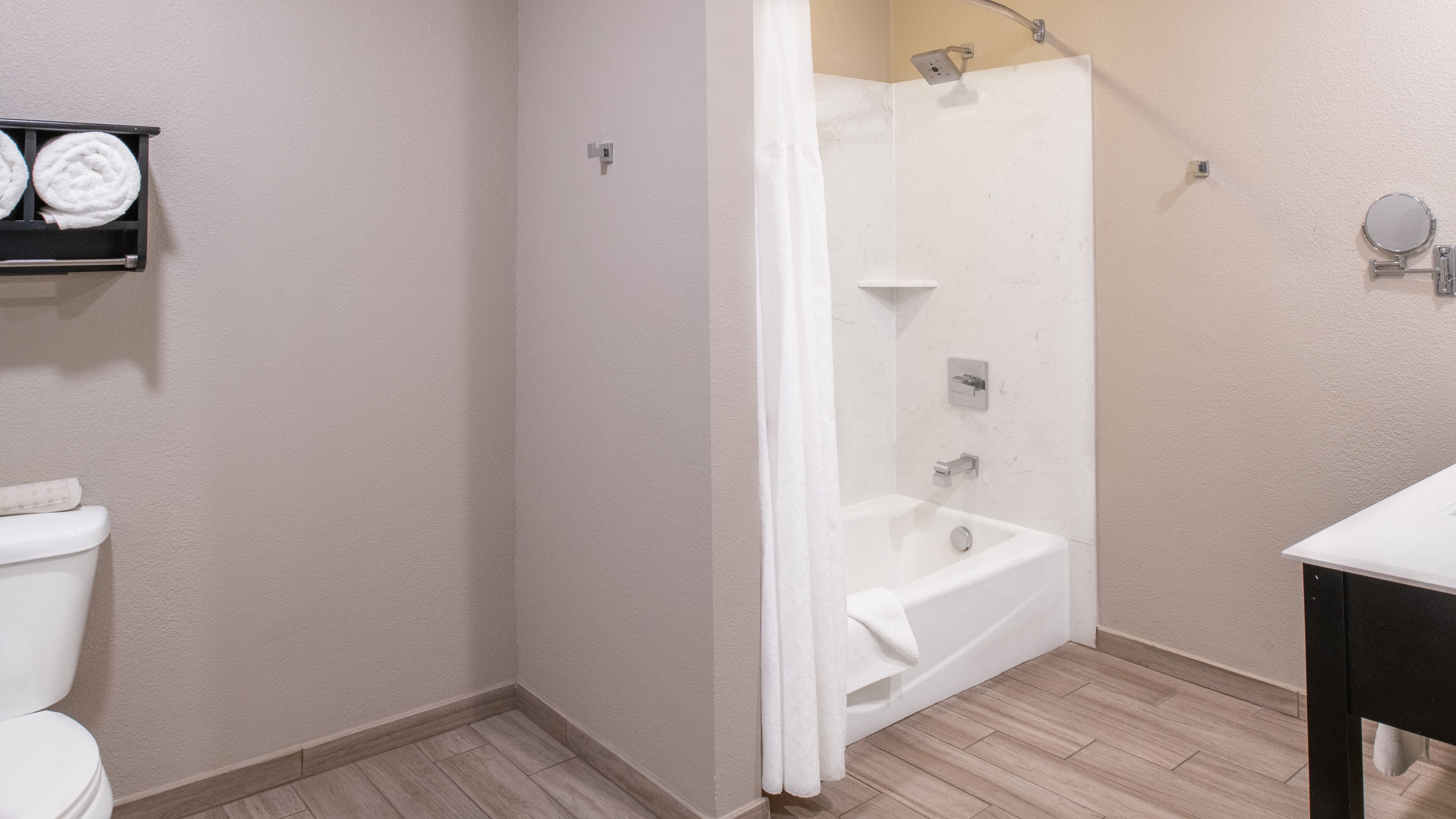 A bathroom with a white bathtub, a shower, and a toilet. There is a towel rack with two towels on the wall.