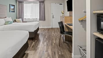 A hotel room with two beds, a desk, a chair, a TV, and a wardrobe.