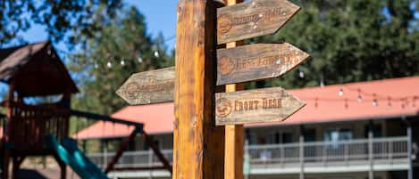 Ein hölzernes Wegweiser mit Pfeilen, die zu verschiedenen Orten zeigen, darunter 'Front Desk' und 'General Store'.