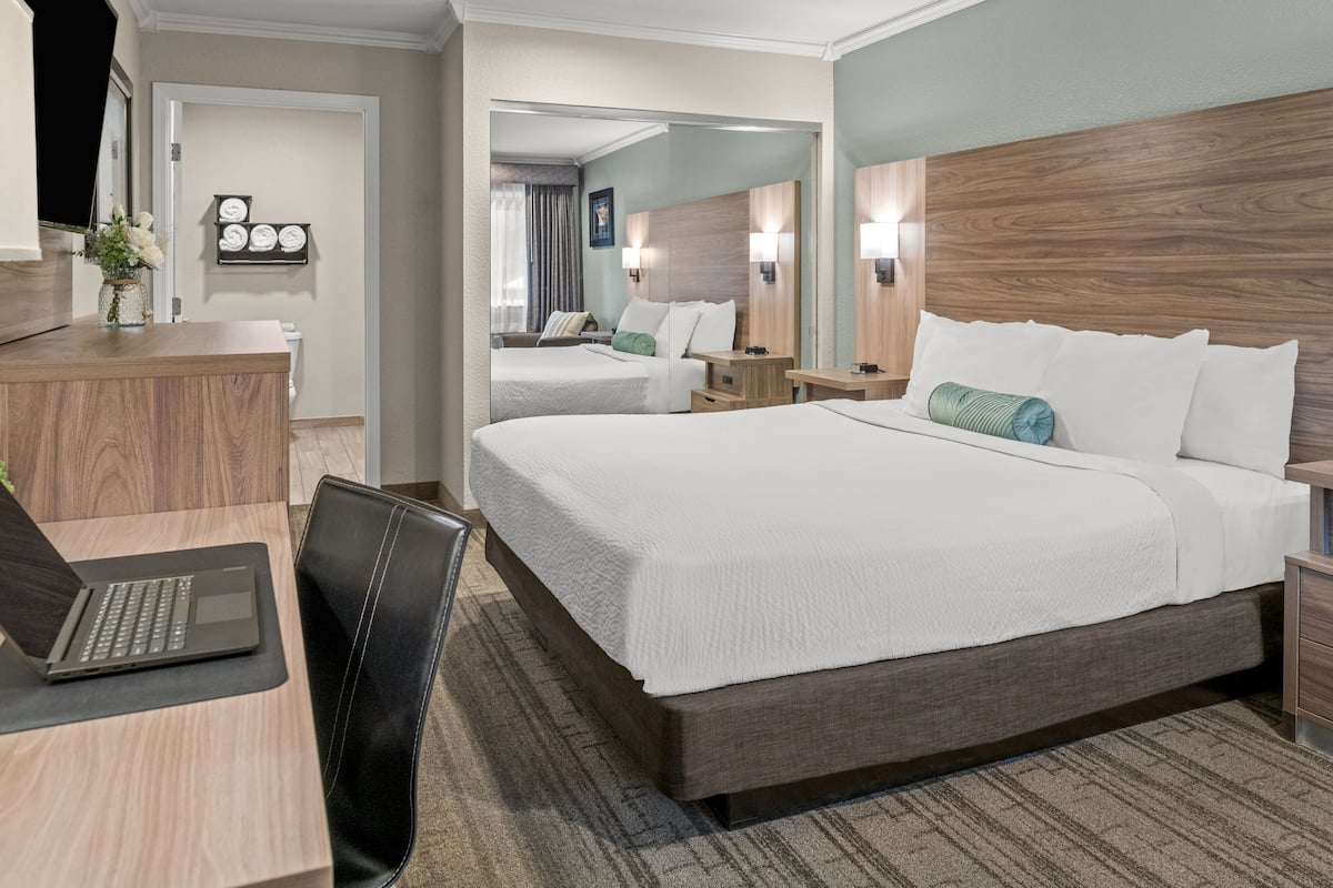 Ein Hotelzimmer mit einem großen Bett, einem Schreibtisch mit einem Laptop, einem Sessel, einem Nachttisch und einem Spiegel.