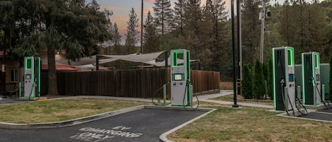 A parking lot with electric vehicle charging stations, a wooden fence, and a building with a red roof in the background.