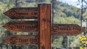 A wooden directional signpost with arrows pointing to 'Yosemite - 12 MI', 'Restaurant', 'Front Desk', and 'General Store'. - Yosemite Westgate Lodge (Groveland)