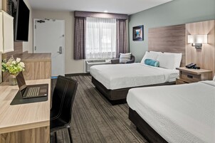 Habitación de hotel con dos camas, un escritorio con una computadora portátil, una silla, un televisor montado en la pared y una ventana con cortinas.