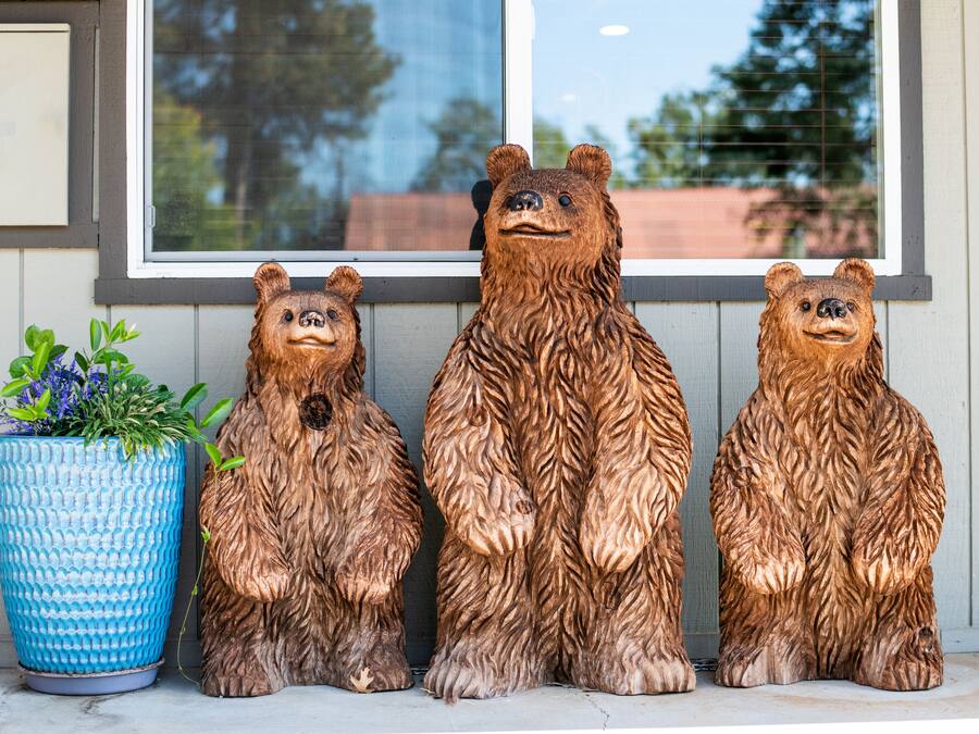 Three wooden bear sculptures on a porch with a blue textured planter to the left.