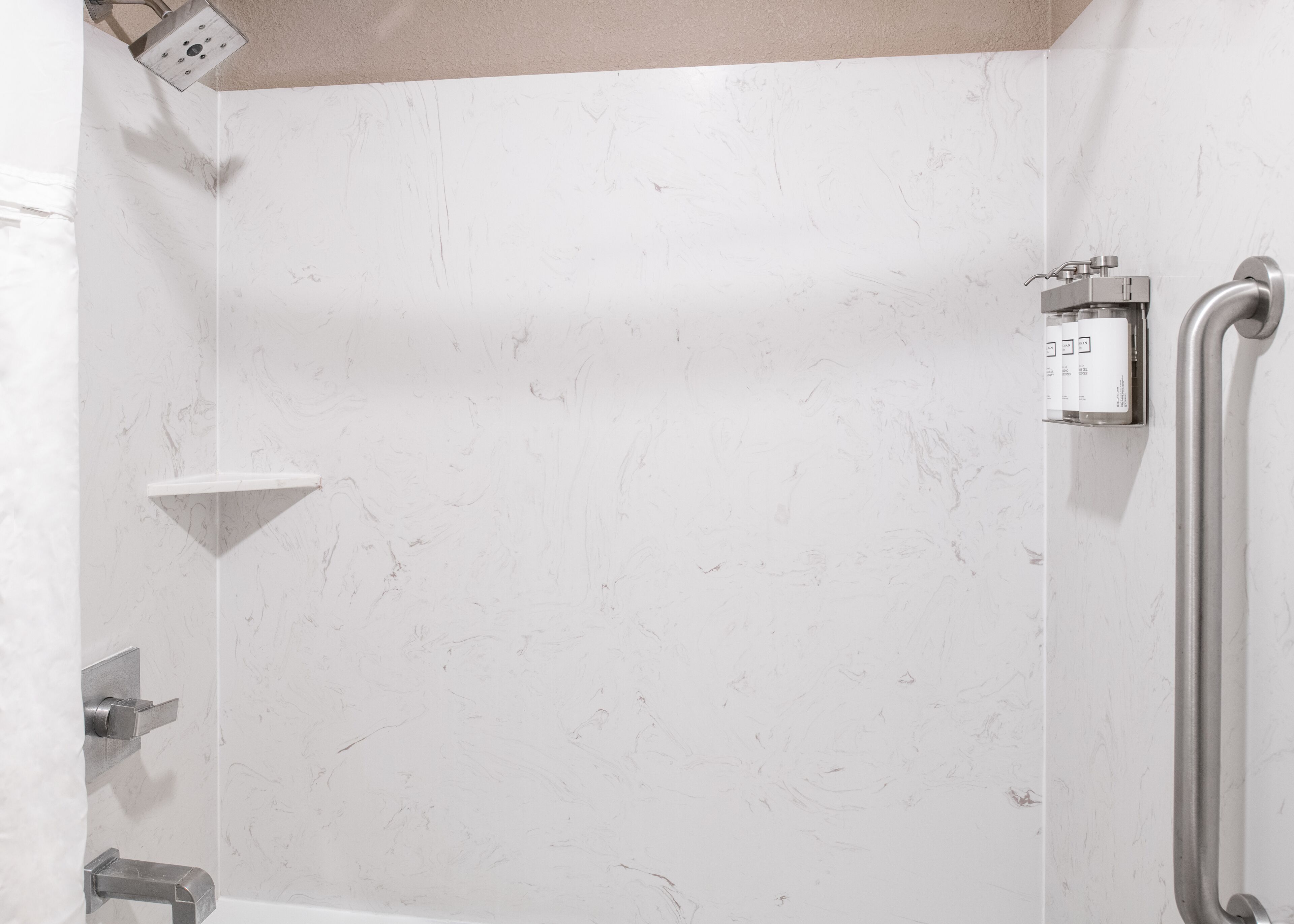 A bathroom with a white marble wall, a handheld showerhead, a grab bar, and a shelf unit.