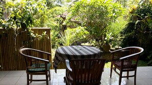 Une terrasse avec une table ronde et deux chaises, entourée d’une végétation luxuriante et d’une clôture en bambou.