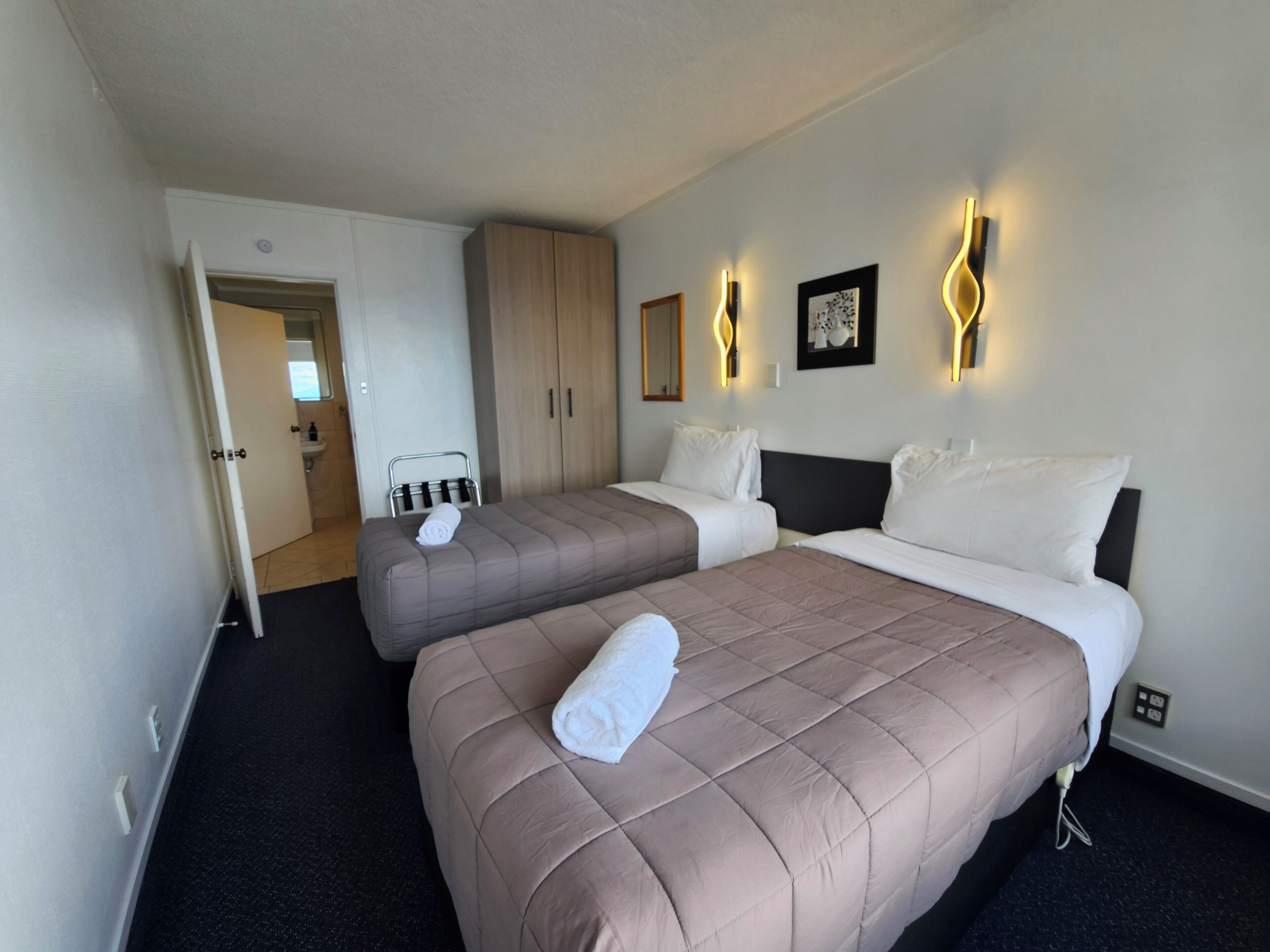 A hotel room with two beds, a wardrobe, a bathroom, and a shower.