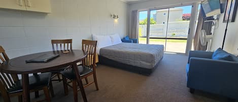 Una habitación con una cama, una mesa con sillas, un sofá, un televisor y una puerta corrediza de vidrio hacia el exterior.