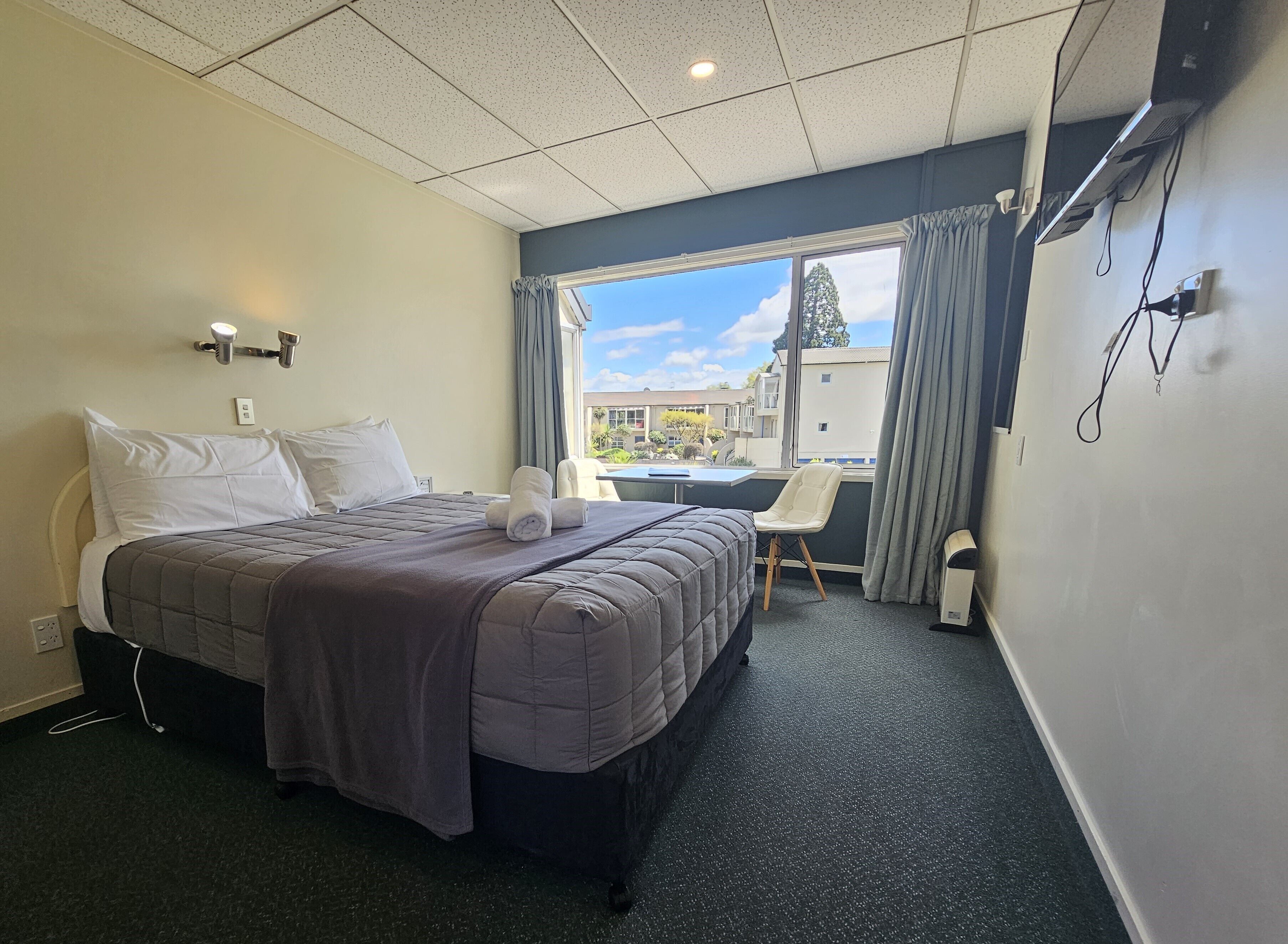 Hotelkamer met een bed, een stoel, een bureau, een raam met uitzicht en een plafond met inbouwverlichting.