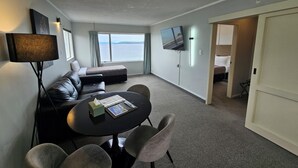 Ein modernes Hotelzimmer mit einer Couch, einem Esstisch, einem Fernseher und Blick auf das Meer.