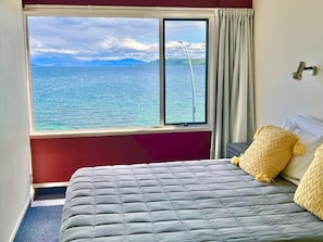 A hotel room with a bed, a window with a view of the sea, and a curtain. - Tui Oaks Motel (Taupo)