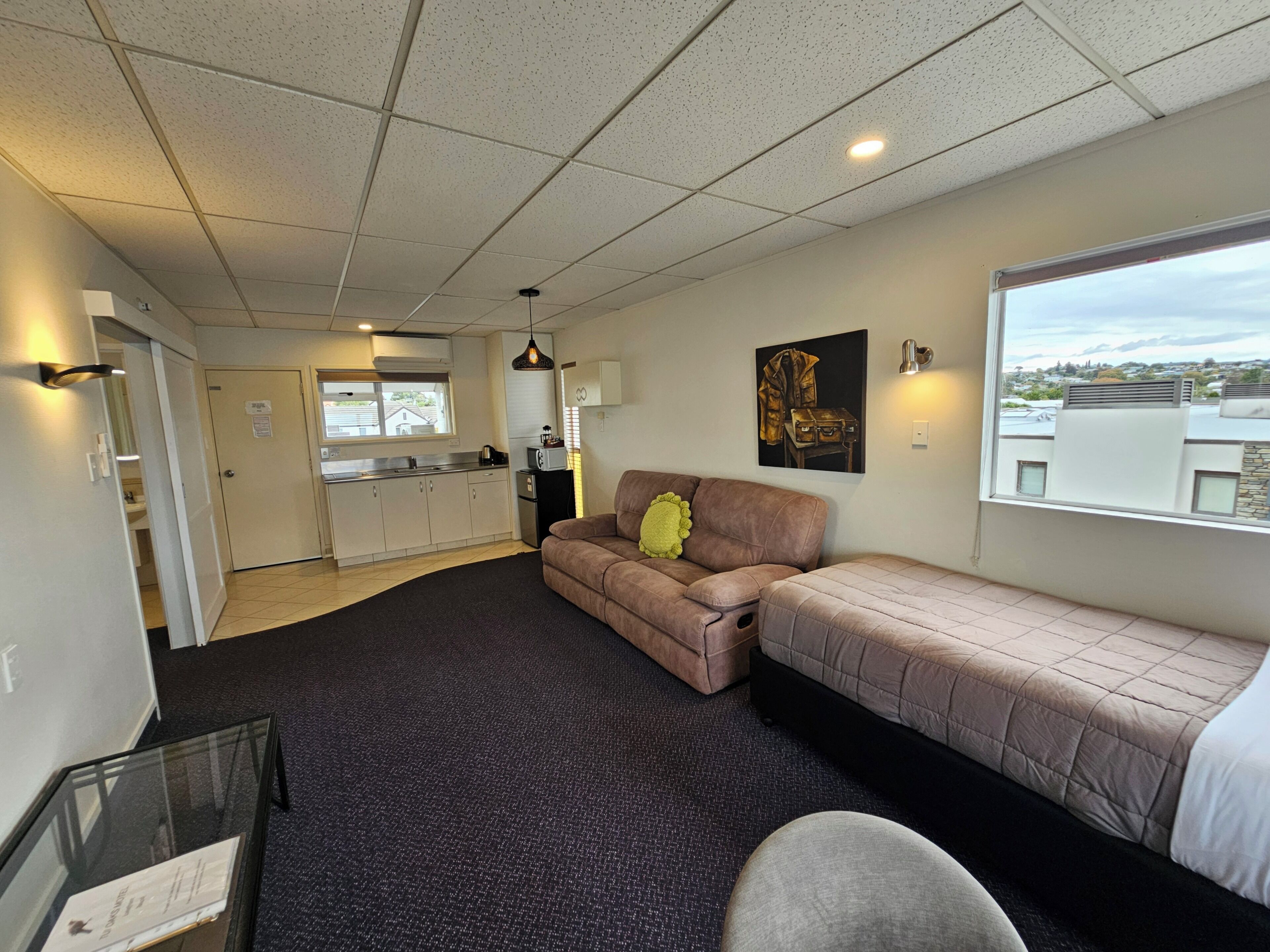 A compact living space with a kitchenette, a sofa, a bed, and a window with a view.