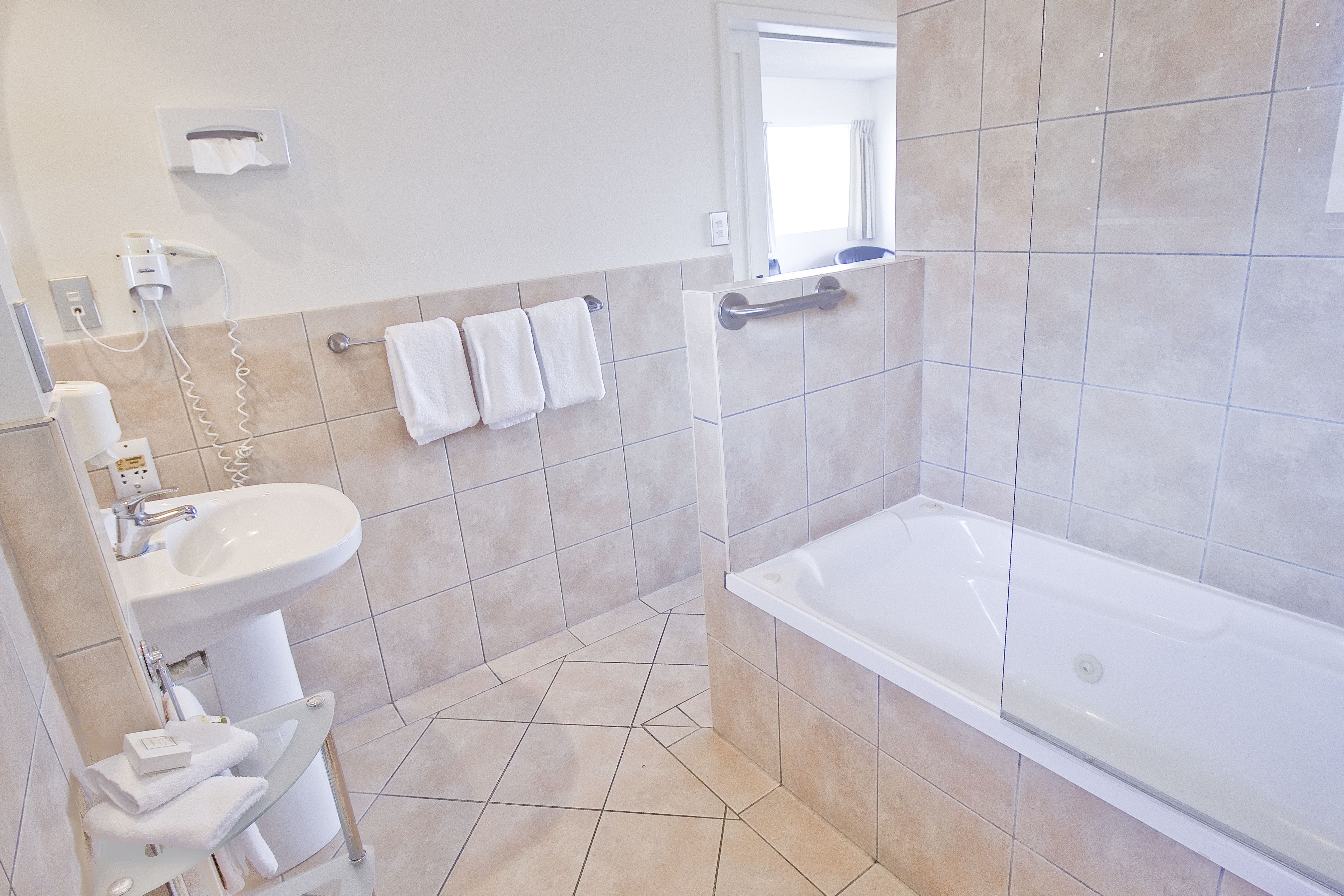A modern bathroom with a sink, mirror, and bathtub. There are towels hanging on the wall and a window providing natural light.