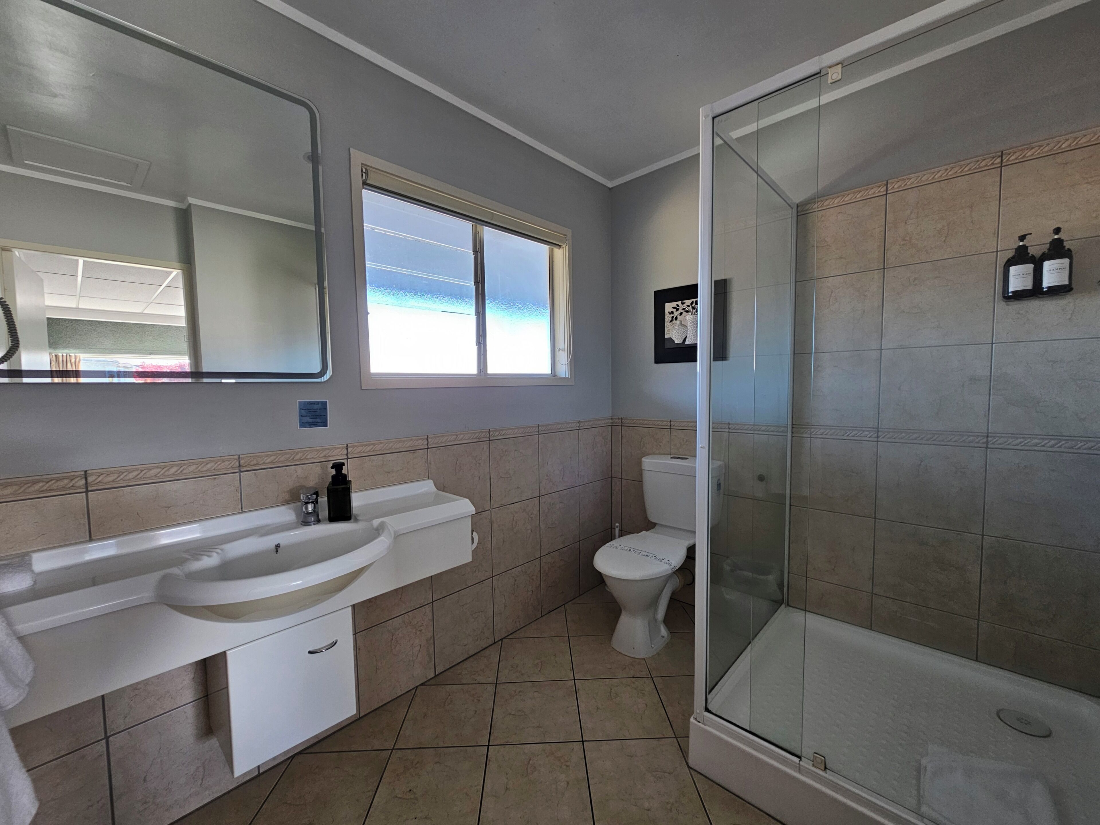 A bathroom with a large mirror, a sink, a toilet, and a shower area.