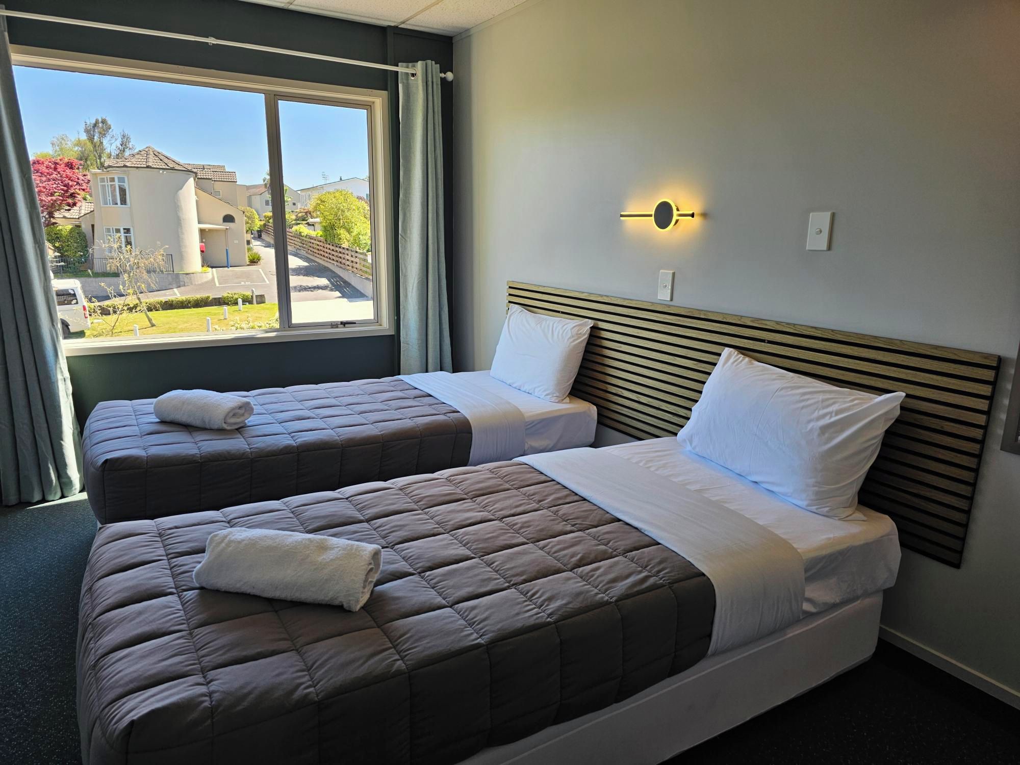 Ein Hotelzimmer mit zwei Betten, einem Fenster mit Vorhängen und einer Wandleuchte.