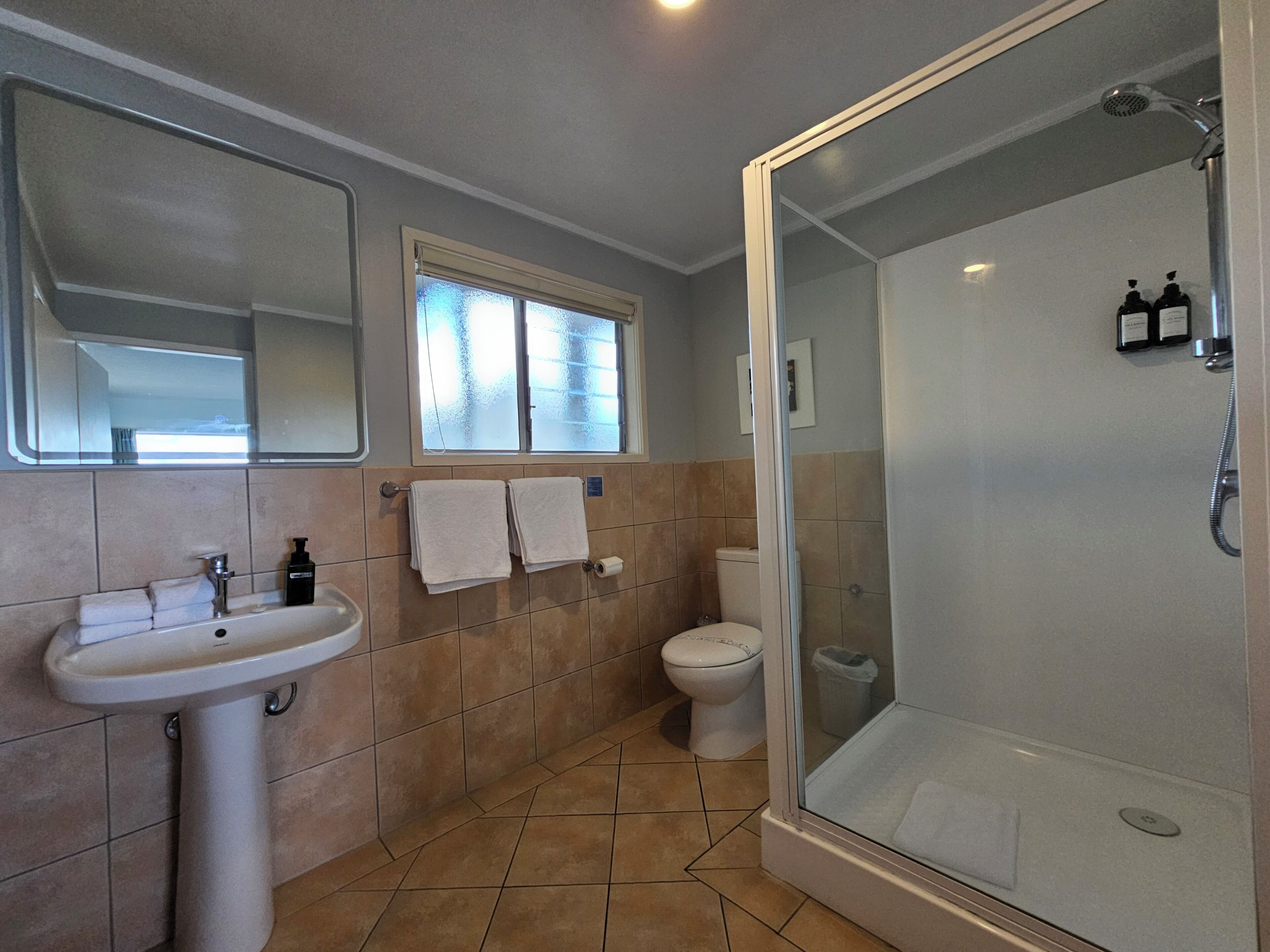 Et badeværelse med vask, toilet og bruser samt et vindue.