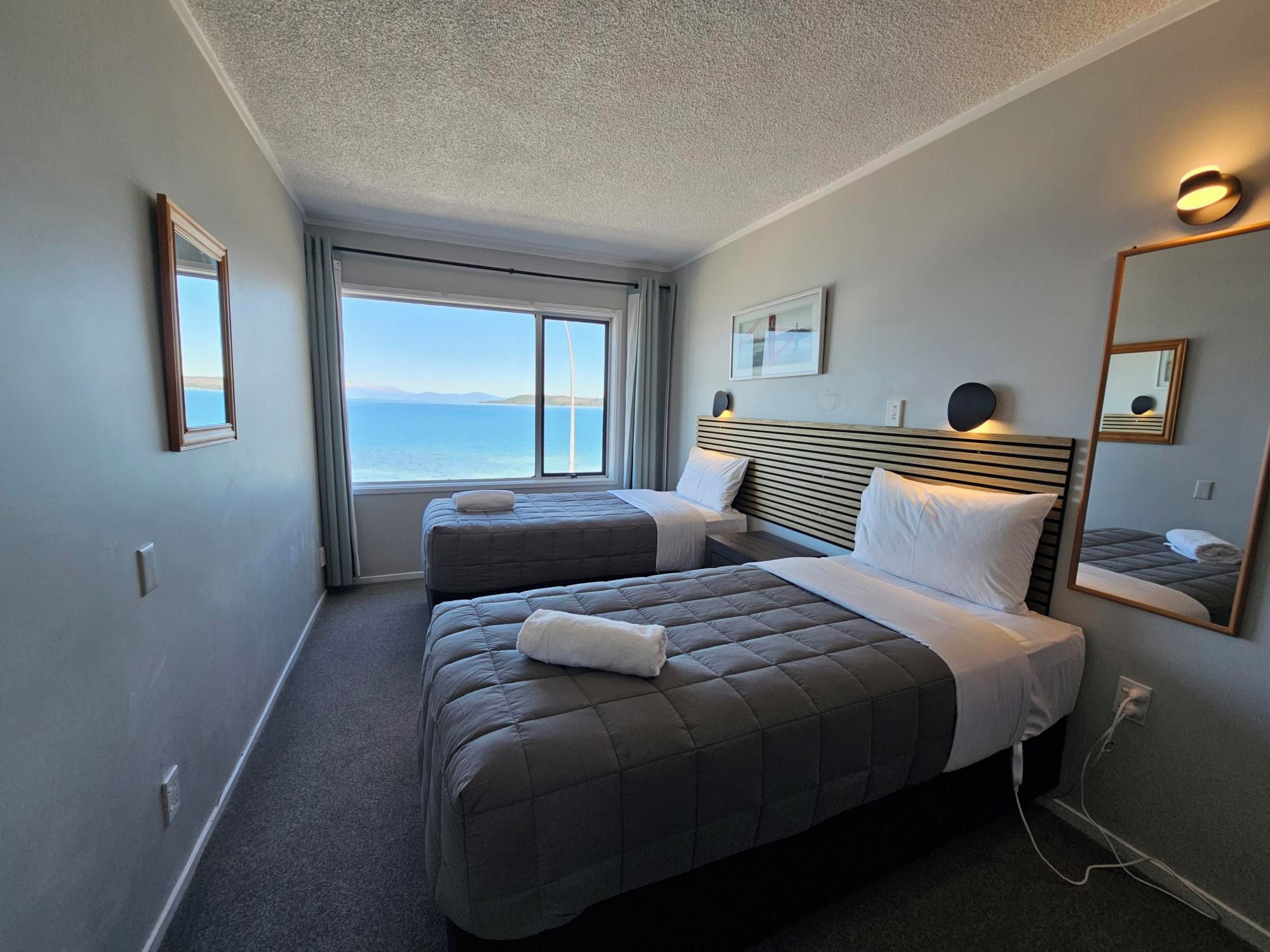 Een hotelkamer met twee bedden, een groot raam met uitzicht op zee en een spiegel aan de muur.