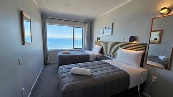 Een hotelkamer met twee bedden, een groot raam met uitzicht op zee en een spiegel aan de muur.