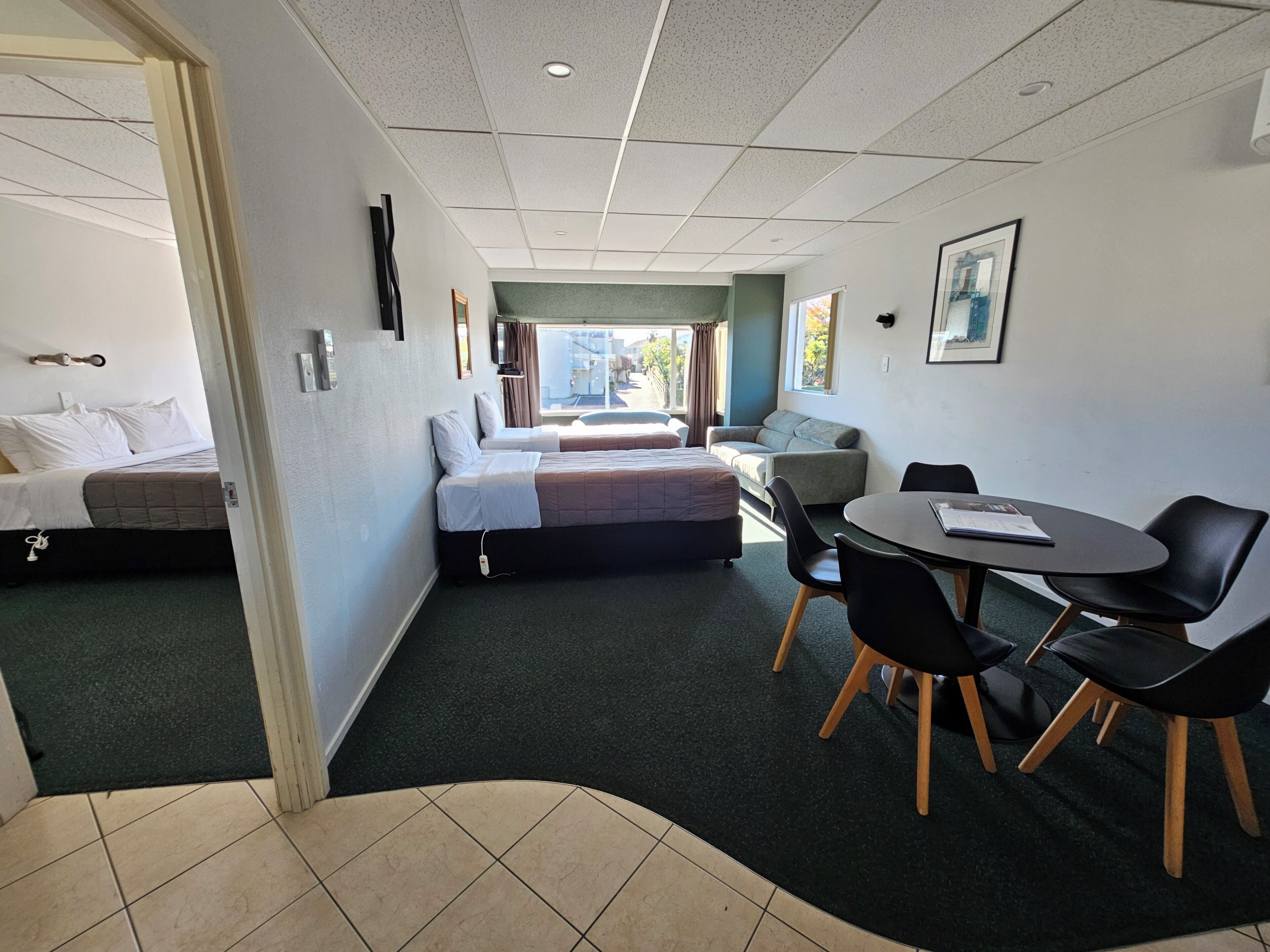Habitación de hotel con cama, sofá, mesa de comedor con sillas y ventana con vistas.