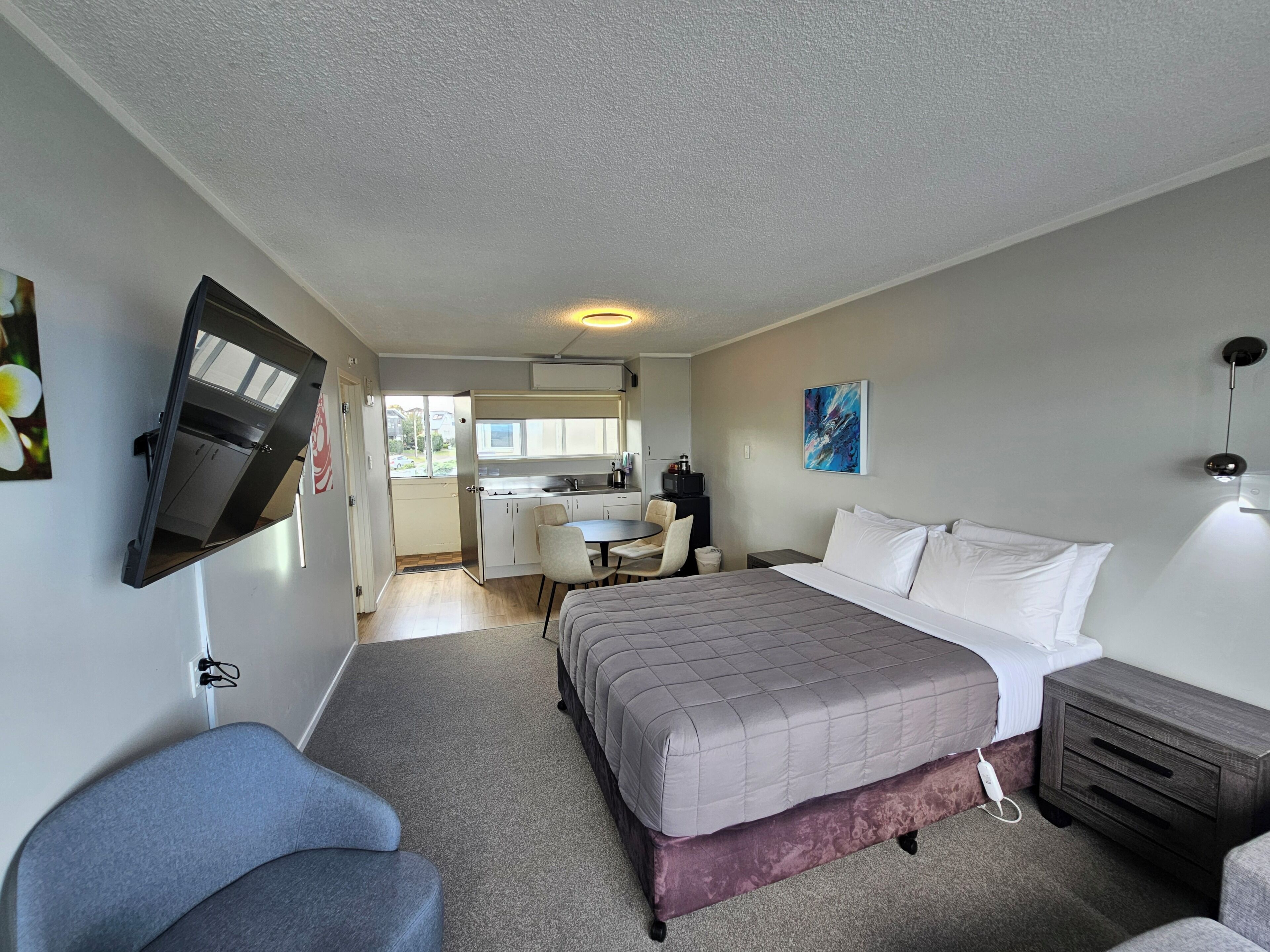 A hotel room with a bed, a desk, a chair, a TV mounted on the wall, and a painting on the wall.