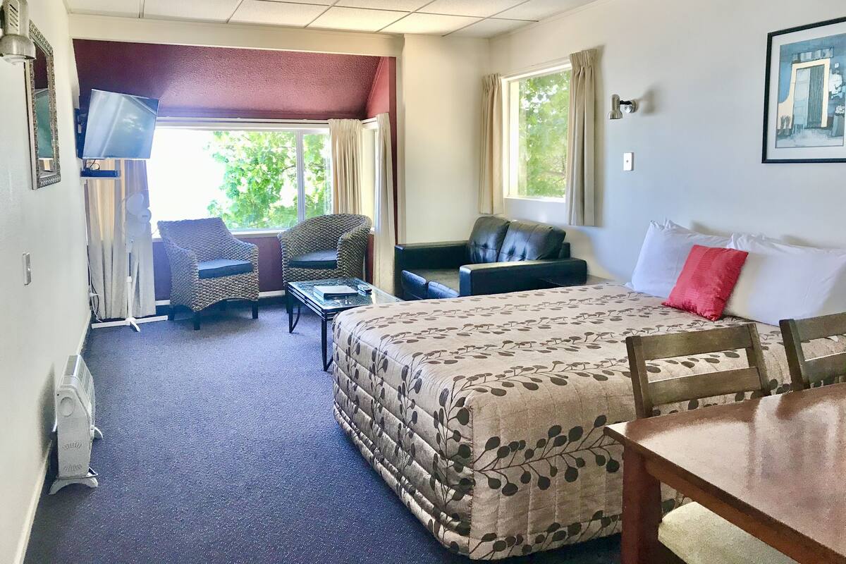 A hotel room with a bed, two armchairs, a sofa, a TV, and a window with curtains.