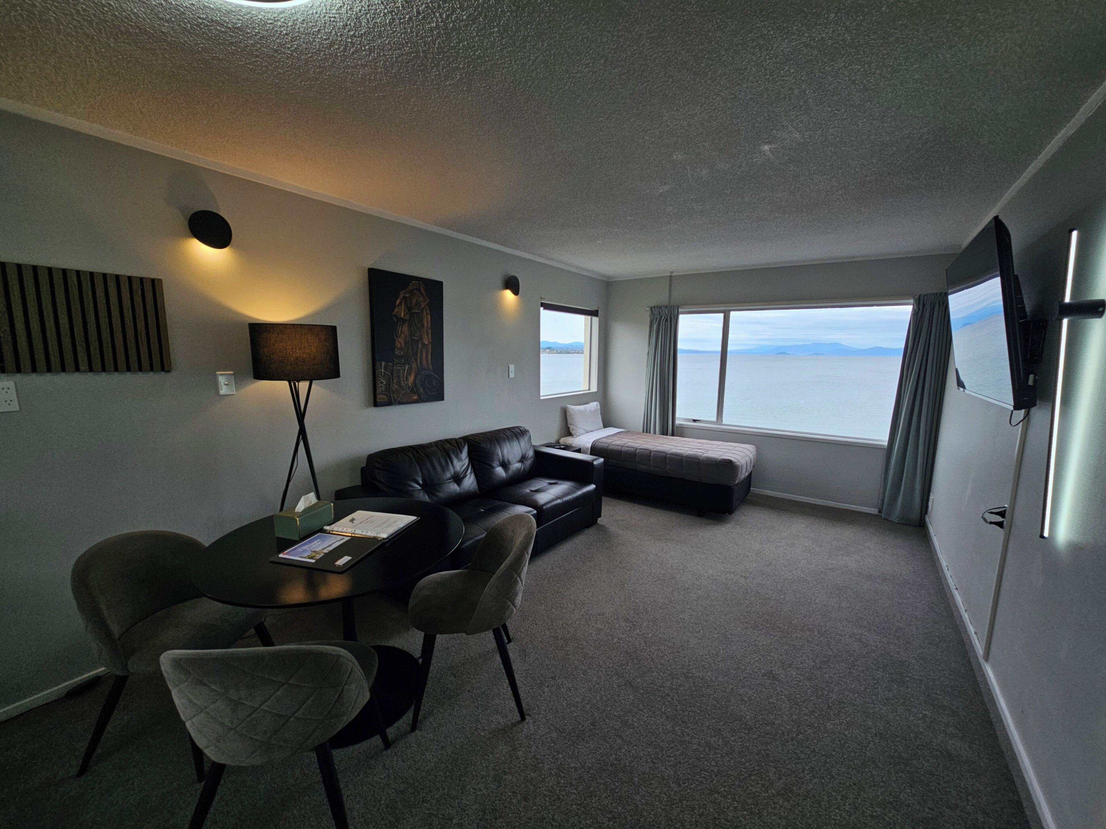 Habitación pequeña con sofá, una mesita y una silla. Ventana con vistas al mar.
