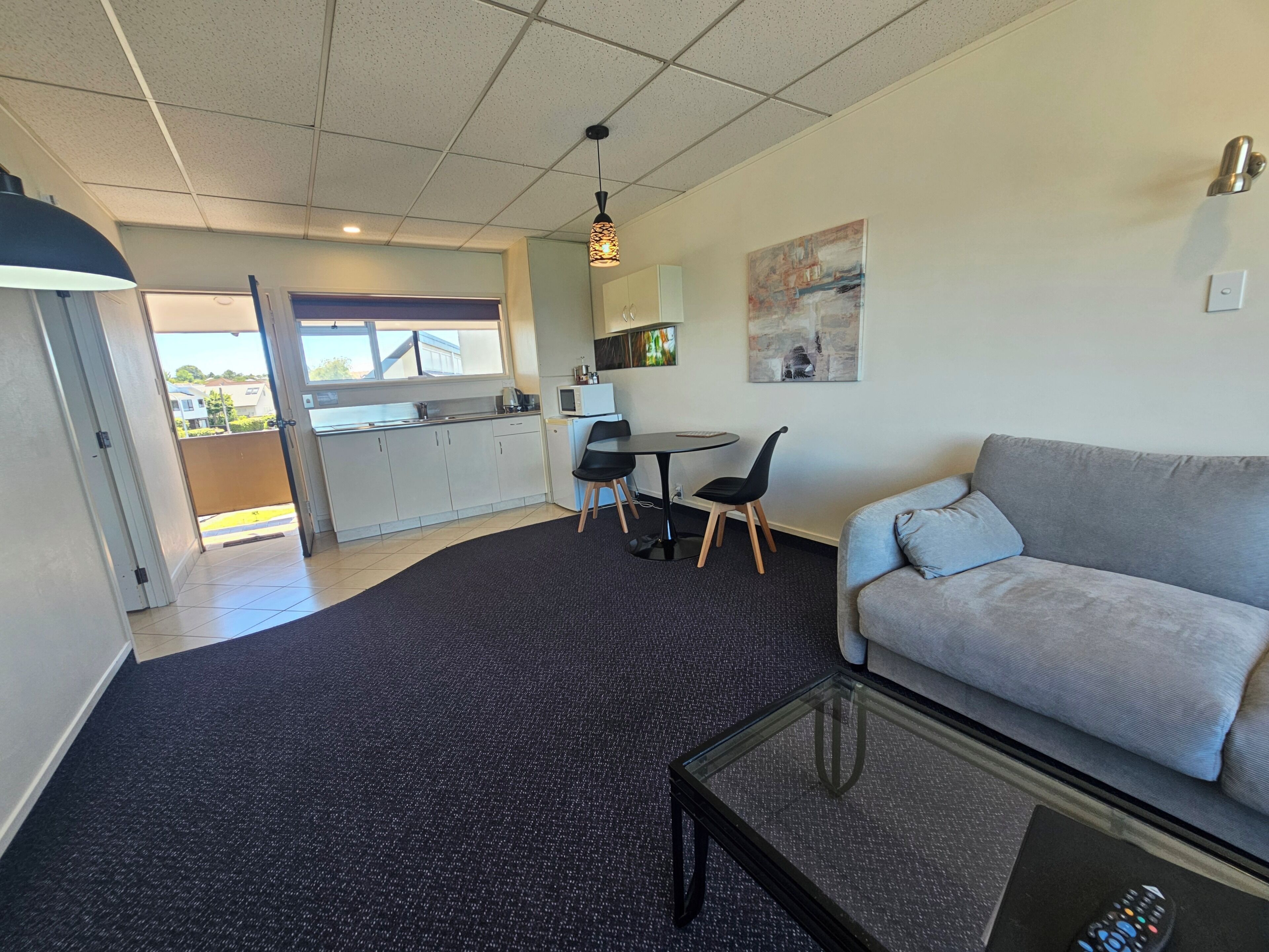 Ein modernes Wohnzimmer mit grauem Sofa, einem Glastisch und einem Essbereich mit kleinem Tisch und Stühlen.