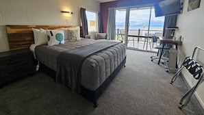 Ein Hotelzimmer mit einem großen Bett, einem Schreibtisch mit Stuhl, einem Fernseher und einem Balkon mit Aussicht.