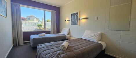 Habitación de hotel con dos camas, un ventanal con cortinas y vistas al exterior, y una lámpara fijada a la pared.