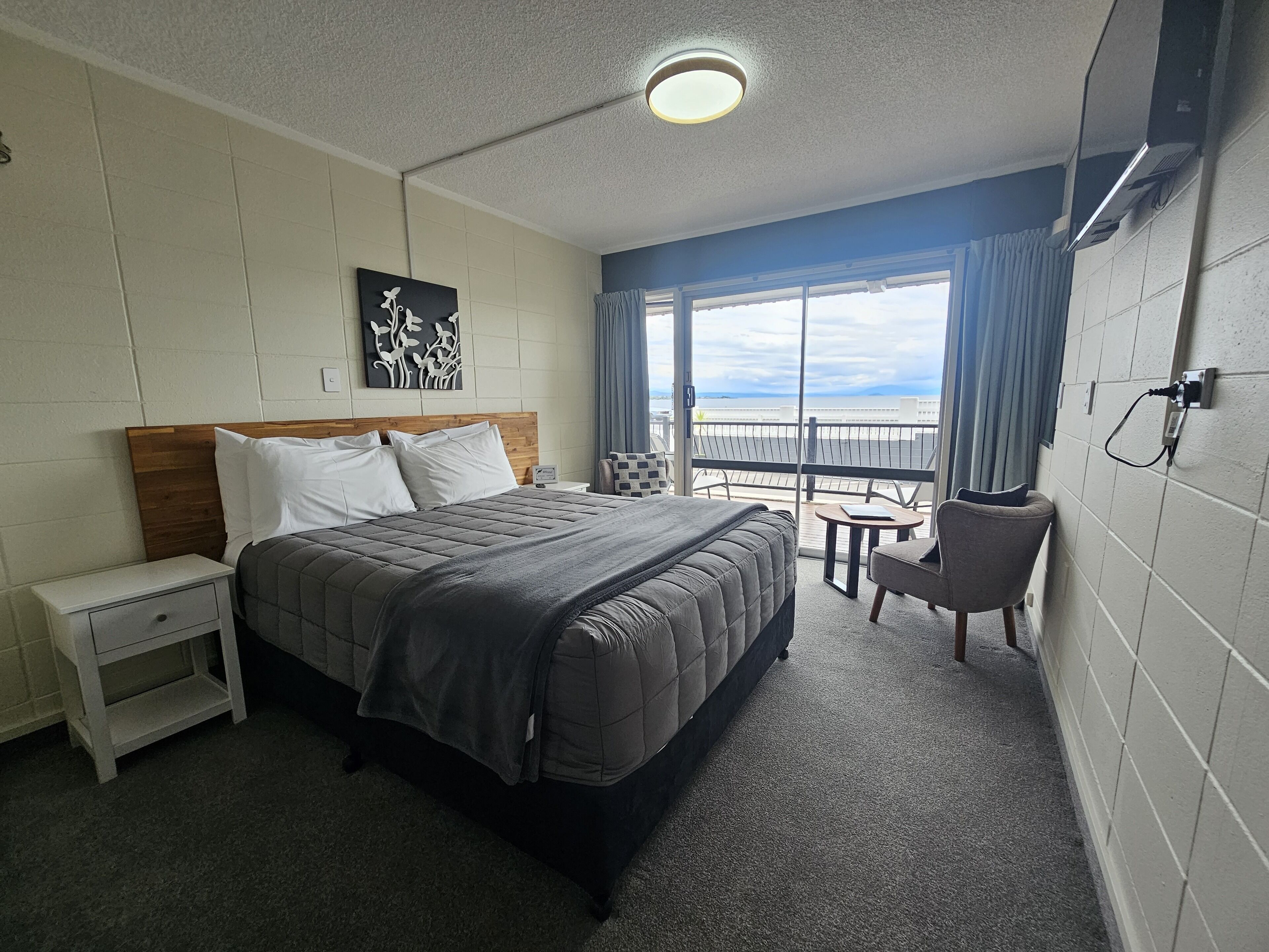 A hotel room with a bed, bedside table, chair, and a balcony with a view.