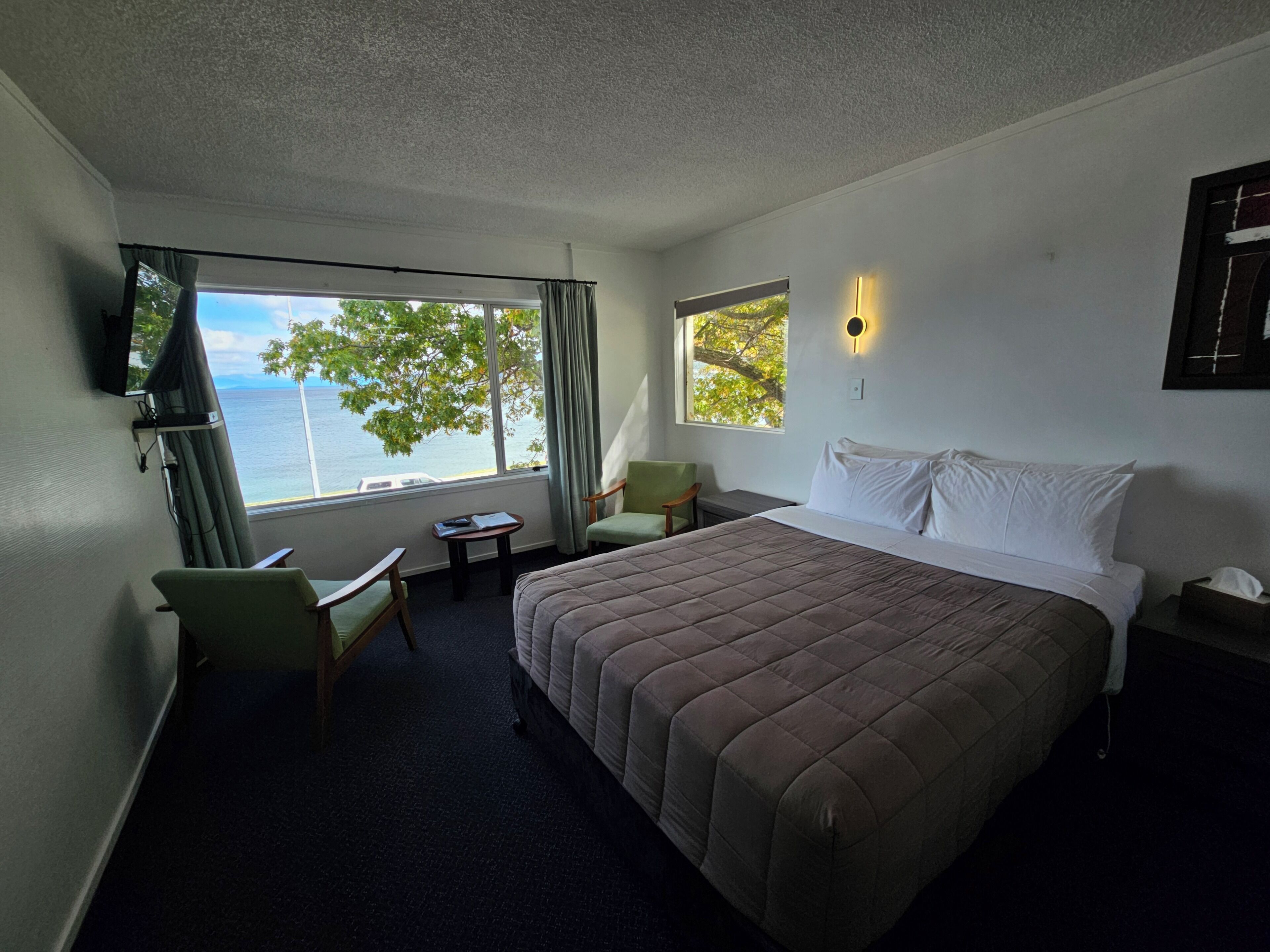 A hotel room with a bed, a desk, a chair, a TV, and a window with a view of the sea.
