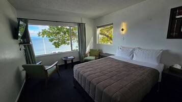A hotel room with a bed, a desk, a chair, a TV, and a window with a view of the sea.