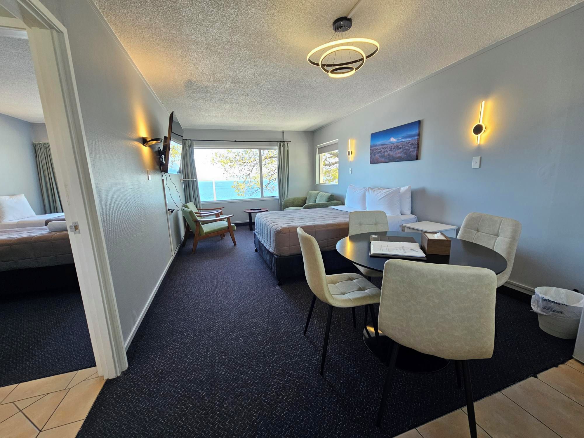 A hotel room with a bed, a desk, a chair, a small table, and a view of the outdoors.