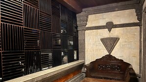 A room with a stone wall, a wooden bench, and a metal grille. - Pande Permai Bungalows (Ubud)