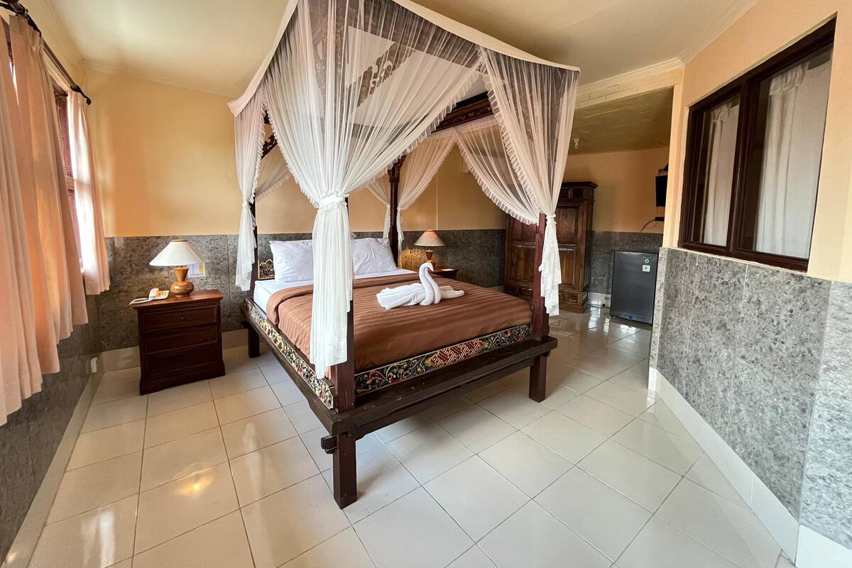 A four-poster bed with a canopy, a bedside table with a lamp, and a swan-shaped towel on the bed.