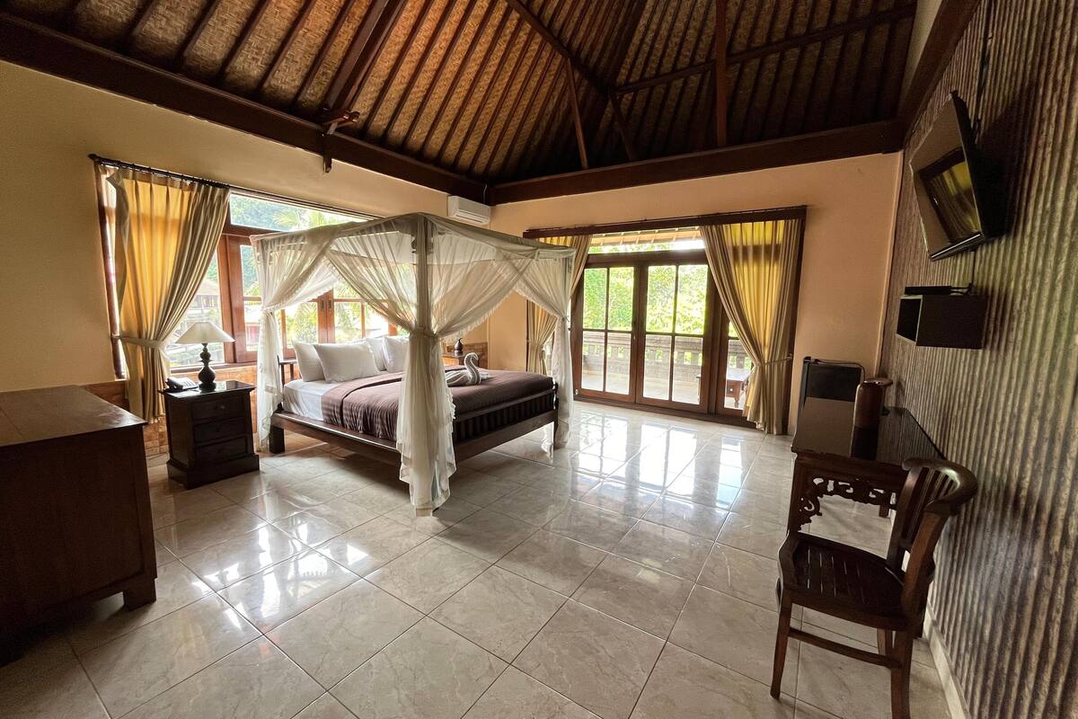 A spacious bedroom with a large bed, a nightstand, a chair, and a TV on the wall.