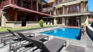 A two-story building with a swimming pool, outdoor seating, and a decorative statue. - Pande Permai Bungalows (Ubud)