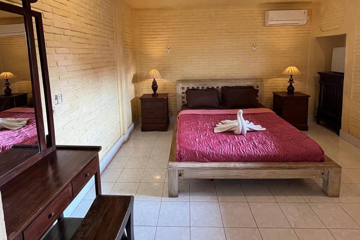 A bedroom with a wooden bed, a ceiling fan, a brick-patterned wall, and a mirror.