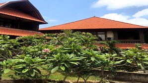 A traditional building with a red tiled roof and a stone wall in the foreground. - Pande Permai Bungalows (Ubud)