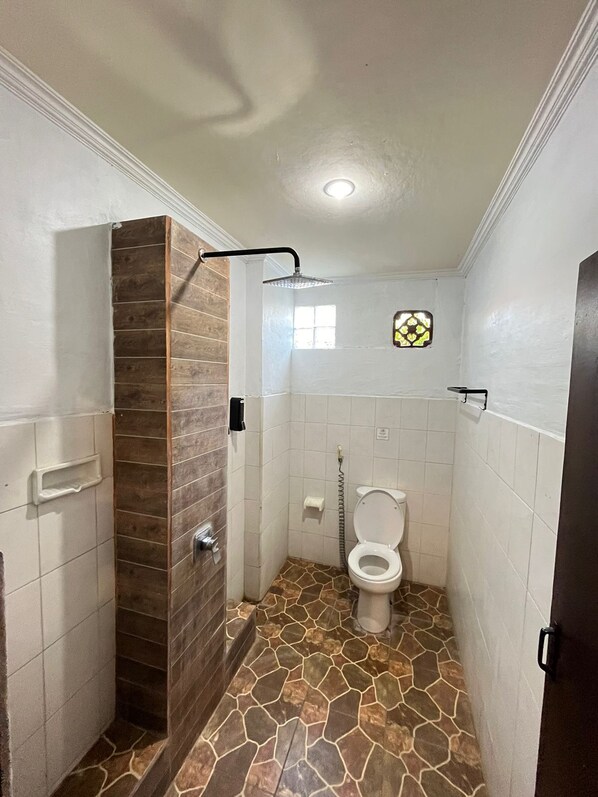 Un baño con ducha, inodoro y un pequeño ventanal.