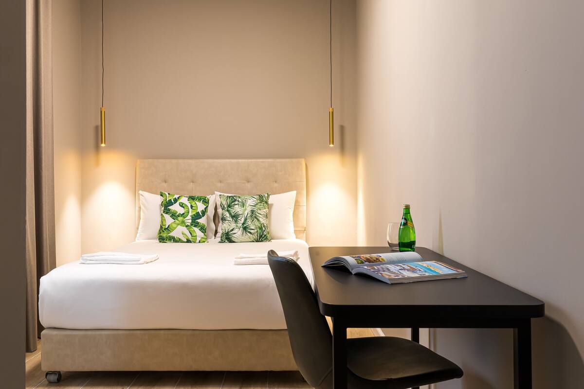 A hotel room with a bed, a table, a chair, and a magazine.
