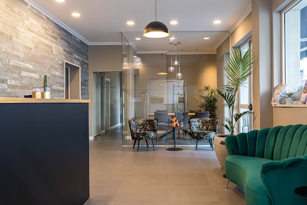 Un área de recepción moderna con un mostrador de madera, un sofá verde y una zona de comedor con sillas y una mesa.