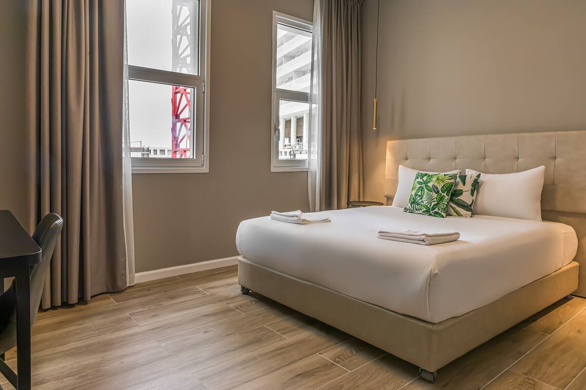 A bedroom with a large bed, two windows, a chair, and a table.