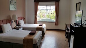 A hotel room with two beds, a desk with a computer, a lamp, and a window with curtains. - Orchid Residence (Koh Samui)