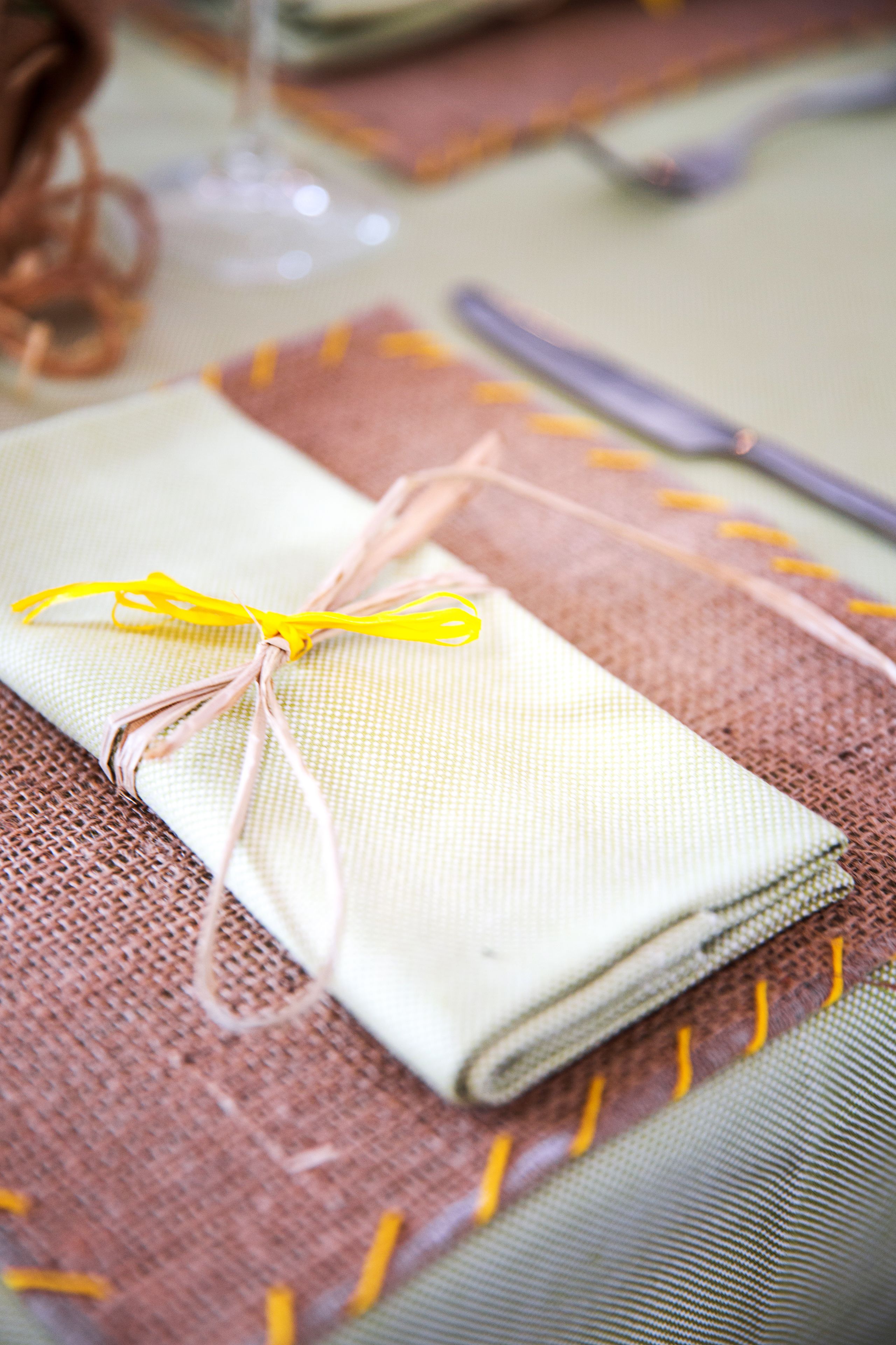 A neatly folded napkin tied with a yellow ribbon on a textured tablecloth.